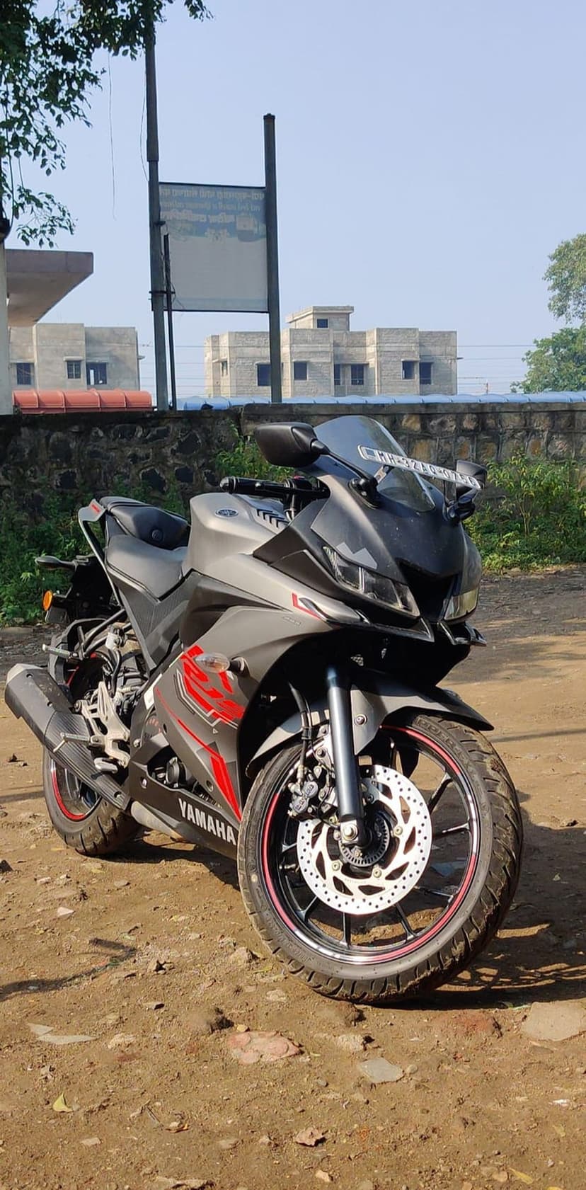 Yamaha R15 V3 motorcycle with gray fairings and red accents parked on a dirt road under a clear blue sky.