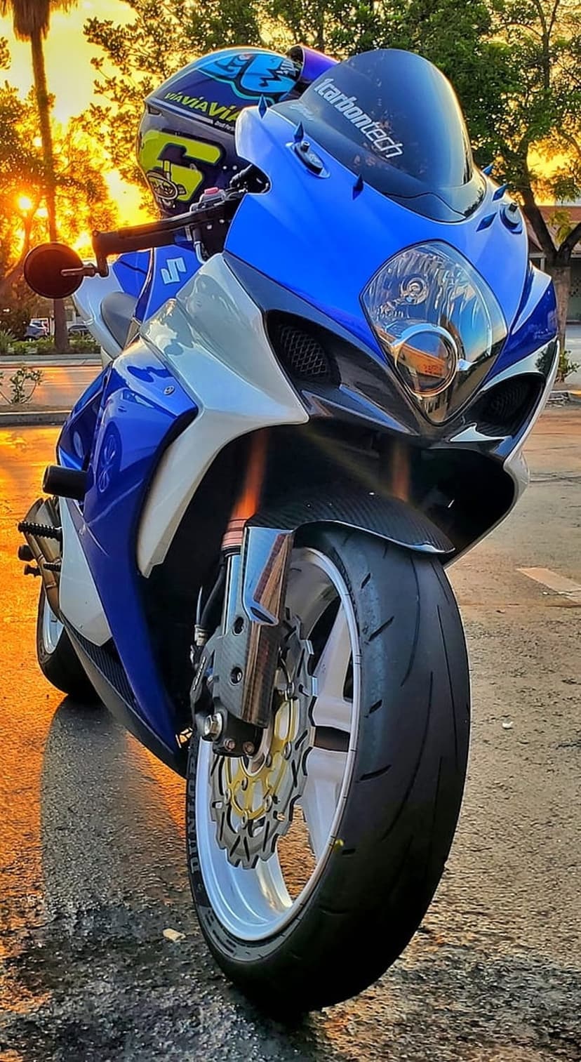 Blue and white Suzuki motorcycle with a helmet on handlebars parked on wet ground during a golden hour sunset.