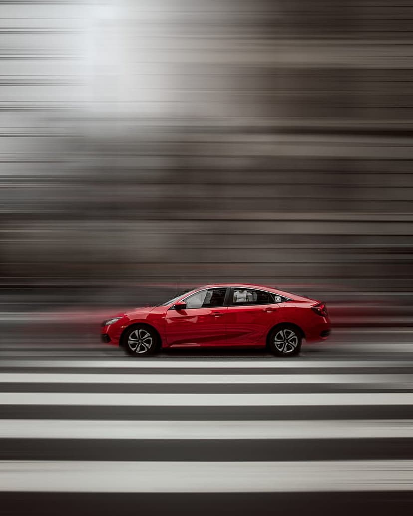 Red sports car blurs past white zebra crossing stripes on a dark asphalt road with cinematic motion effects.