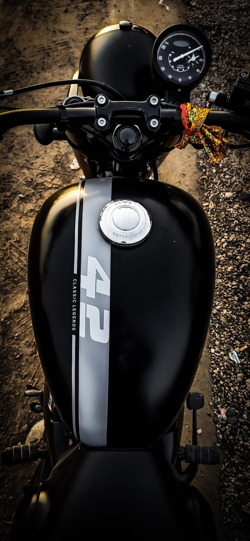 Black Jawa 42 motorcycle seen from above showing the fuel tank, chrome cap, and handlebars on a gravel path.