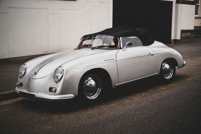 Silver Porsche 356 convertible with a black soft top parked on a street, showcasing vintage chrome trim and curves.