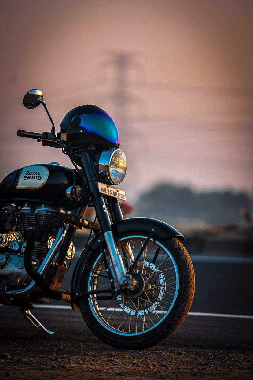 Royal Enfield motorcycle on a dirt road at sunset with a blue helmet resting on the chrome handlebars.