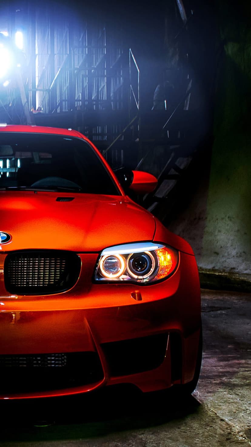 Orange BMW M Series coupe showcases aggressive halo headlights and a signature kidney grille in a dark setting.