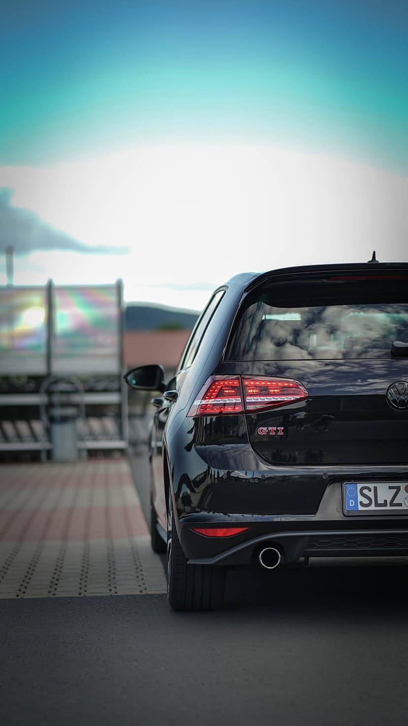 Black Volkswagen Golf GTI rear view featuring glowing red taillights on pavement beneath a vivid twilight sky.