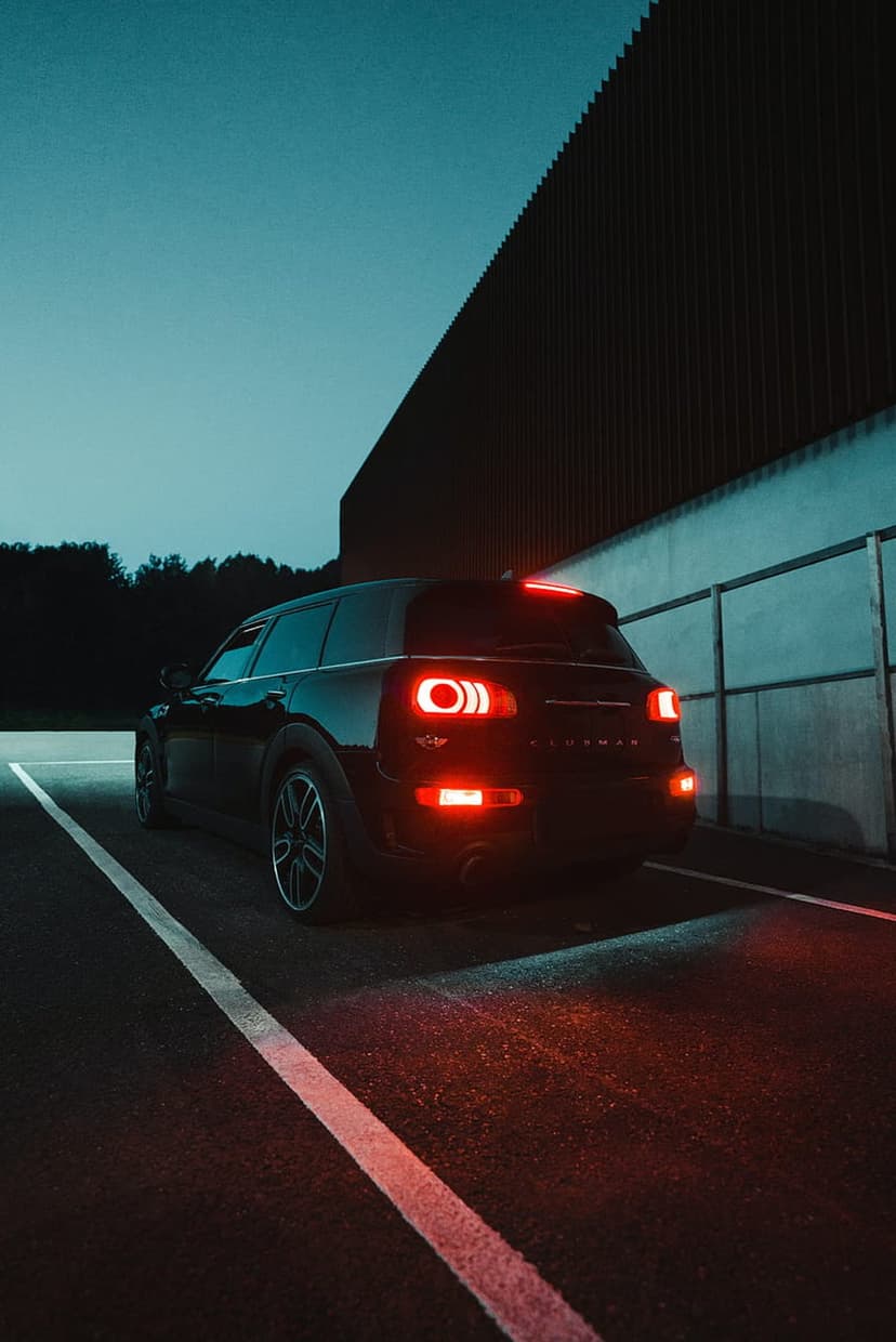 Mini Cooper Countryman rear lights glowing red in a dark parking lot next to a modern building at dusk.