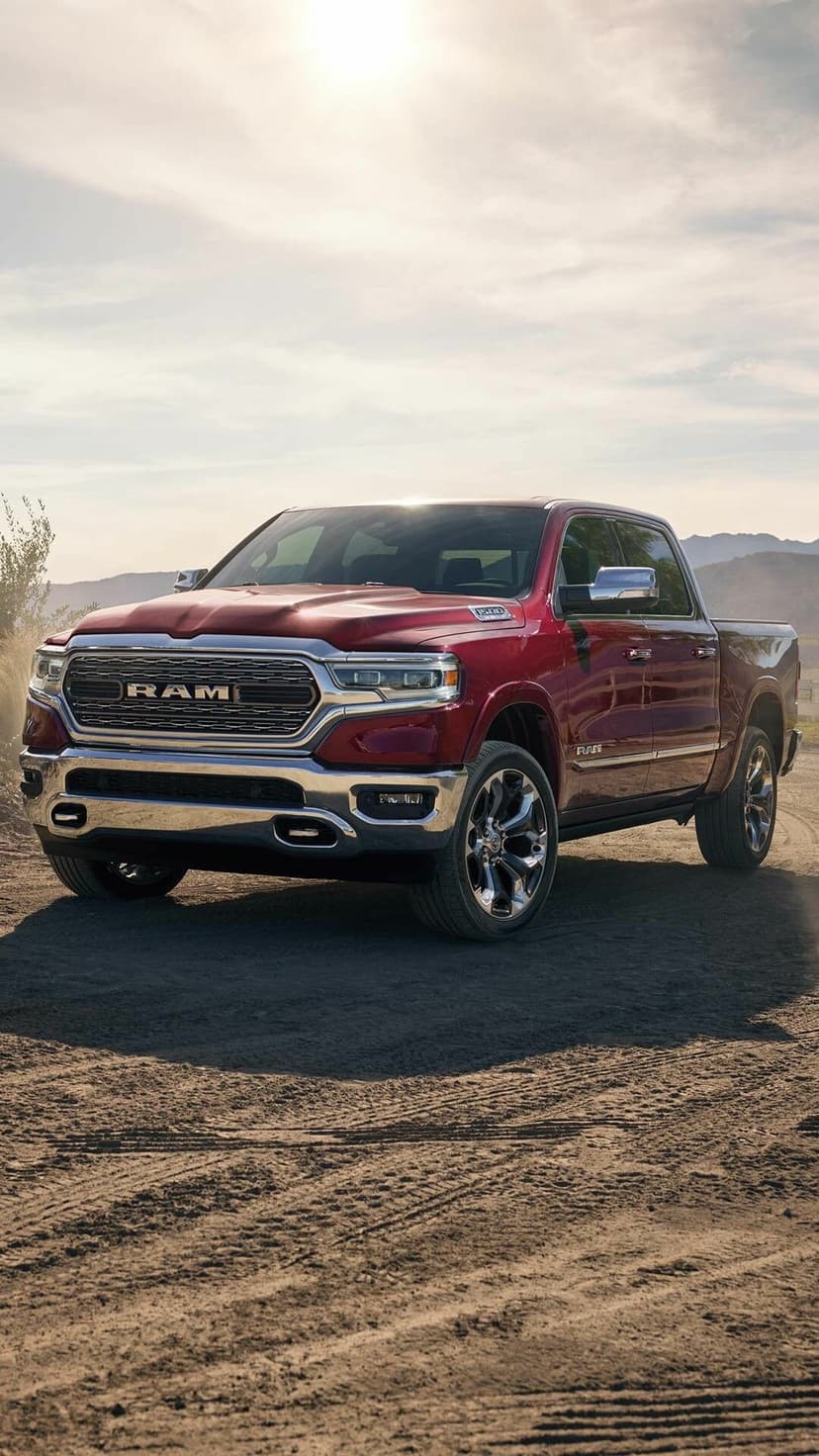 Red Ram 1500 pickup truck on a dirt road with chrome accents and distant mountains under a hazy sky.