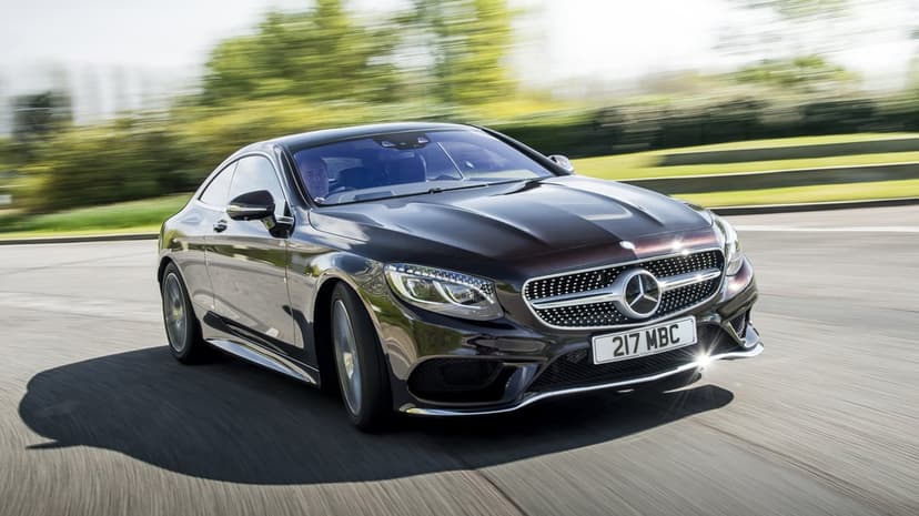 Dark Mercedes-Benz coupe driving fast on a curved road with blurred green trees and sunlight reflections.