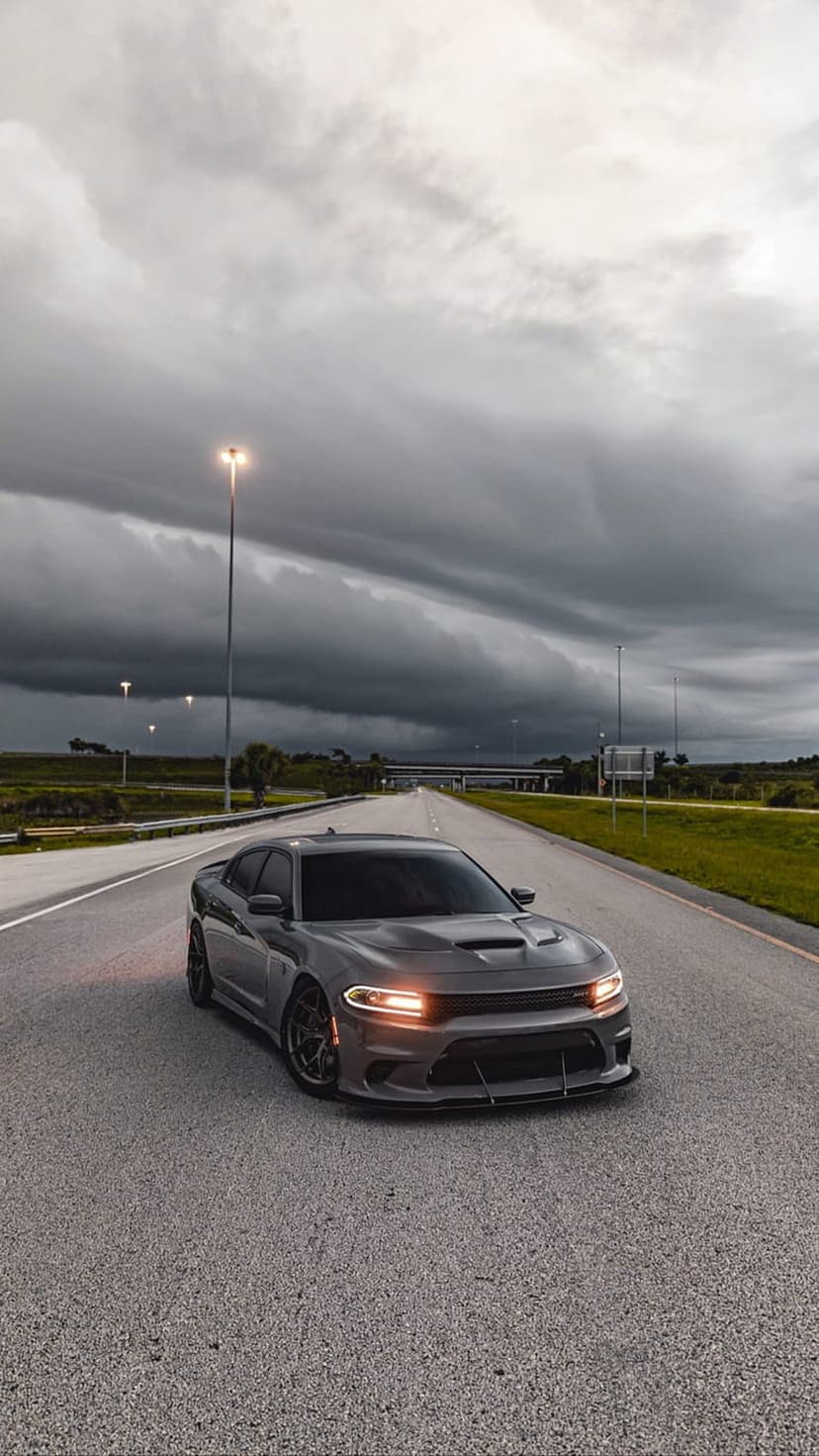 Dodge Charger on a dark highway beneath a heavy stormy sky with glowing headlights in a vertical view.