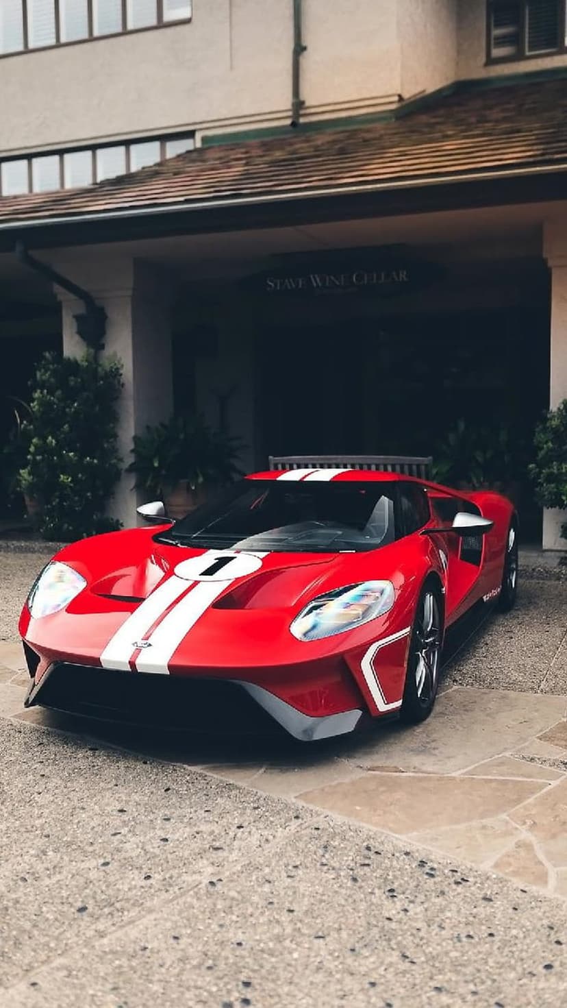 Red Ford GT race car with white stripes and number 1 on the hood parked in front of a stone wine cellar building.
