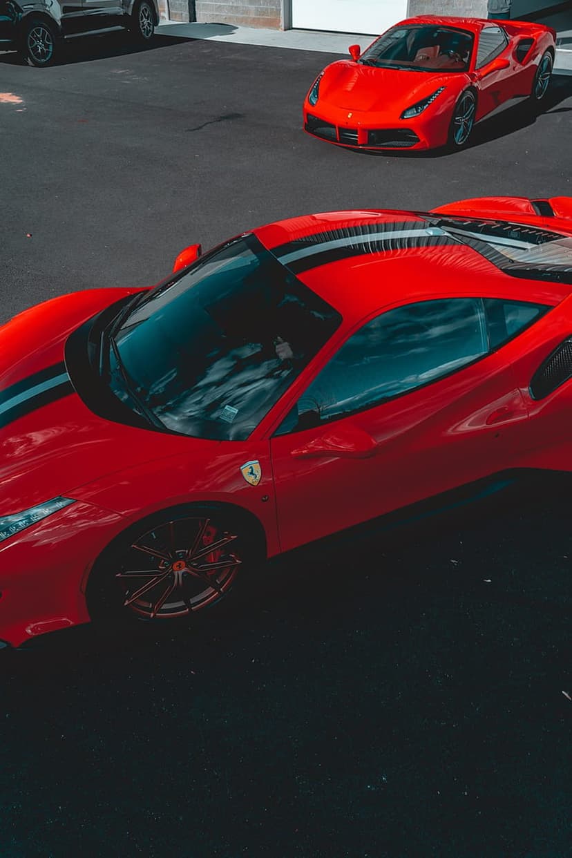 Red Ferraris with white racing stripes parked on dark asphalt under a reflective sky in vertical orientation.