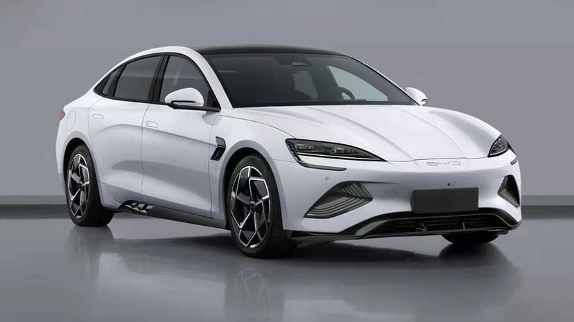 Front three-quarter view of a white electric sedan with a black glass roof in a minimalist grey studio.