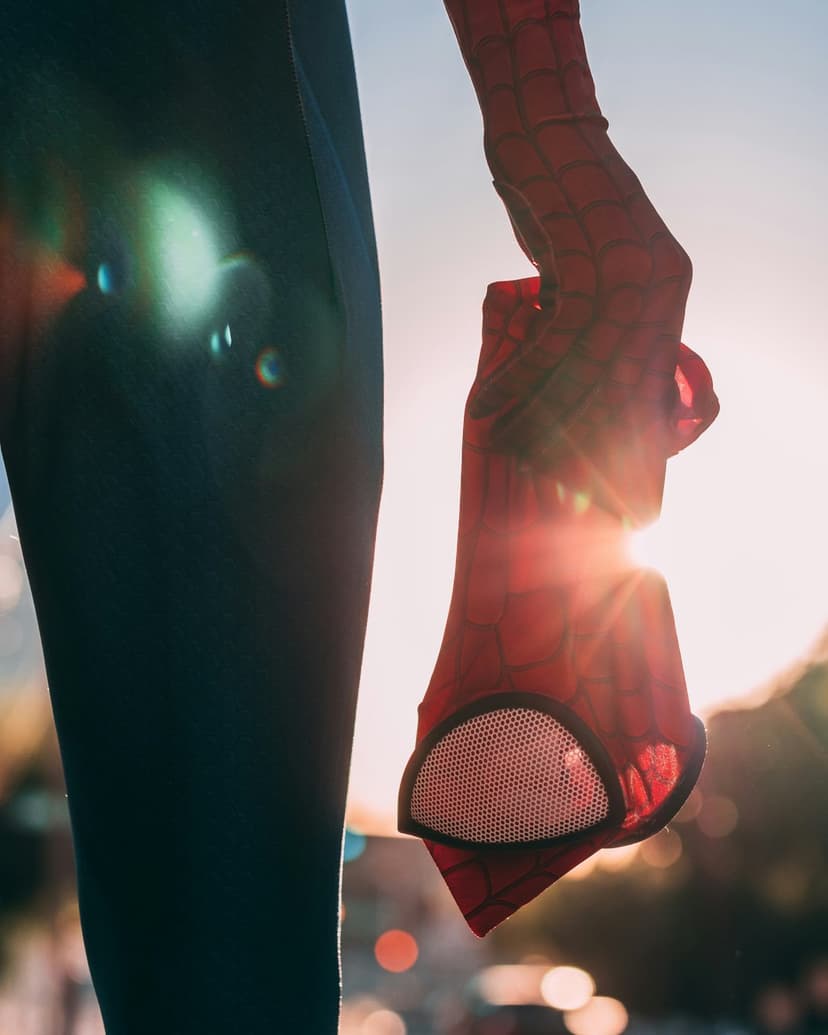 Spider-Man's red and black gloved hand reaches toward the viewer with golden sunlight creating a bright lens flare.
