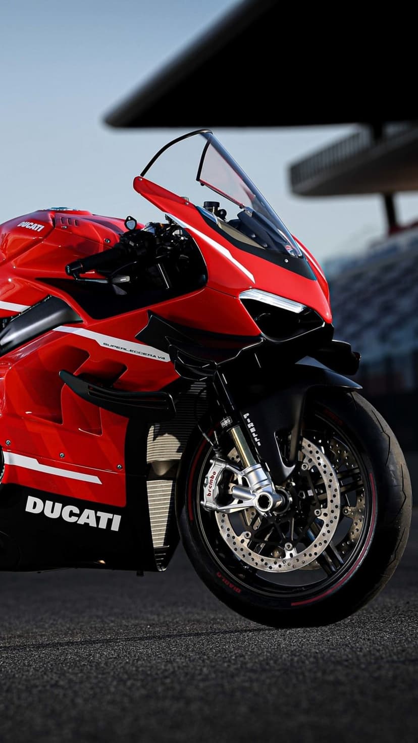 Red Ducati Superleggera V4 motorcycle with carbon fiber details and Brembo brakes on a sunny racetrack.