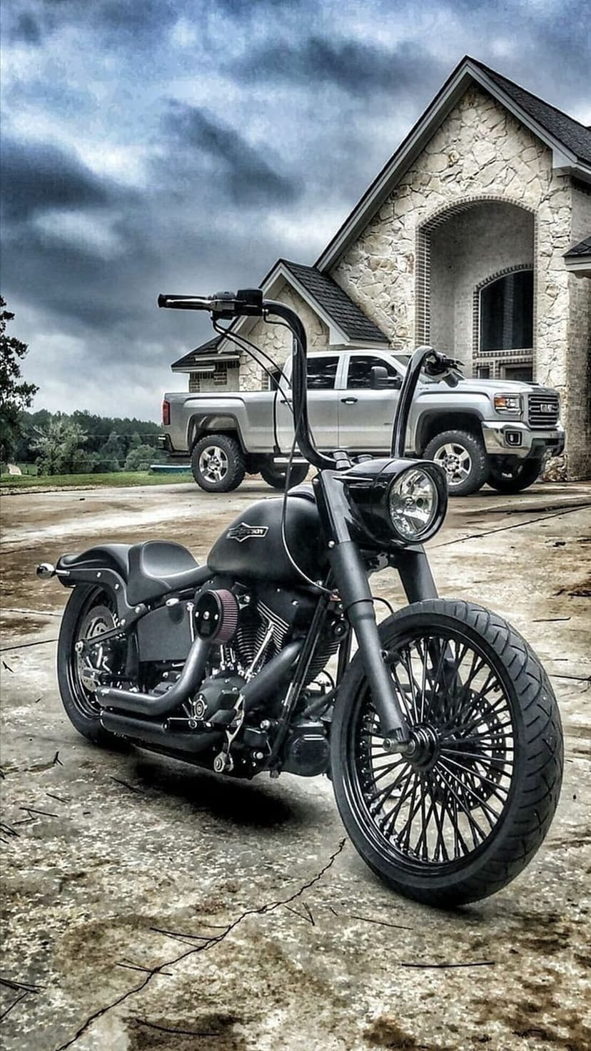 Custom black Harley-Davidson motorcycle parked on a driveway with a silver GMC truck and stone house behind it.