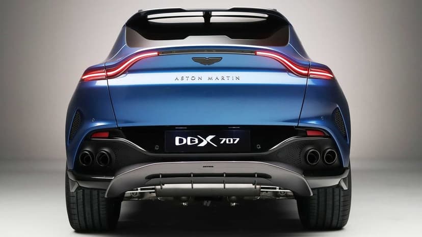 Rear view of a blue Aston Martin DBX 707 SUV with glowing LED taillights and quad exhaust in a studio setting.