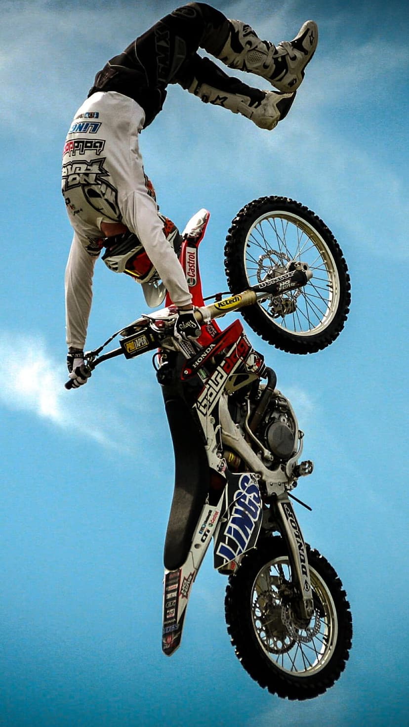 Motocross rider performs an inverted backflip on a dirt bike against a clear blue sky during an FMX jump.