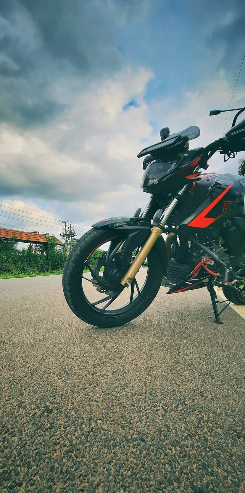 TVS Apache RTR 160 4V motorcycle parked on asphalt under grey storm clouds with green trees in the background.