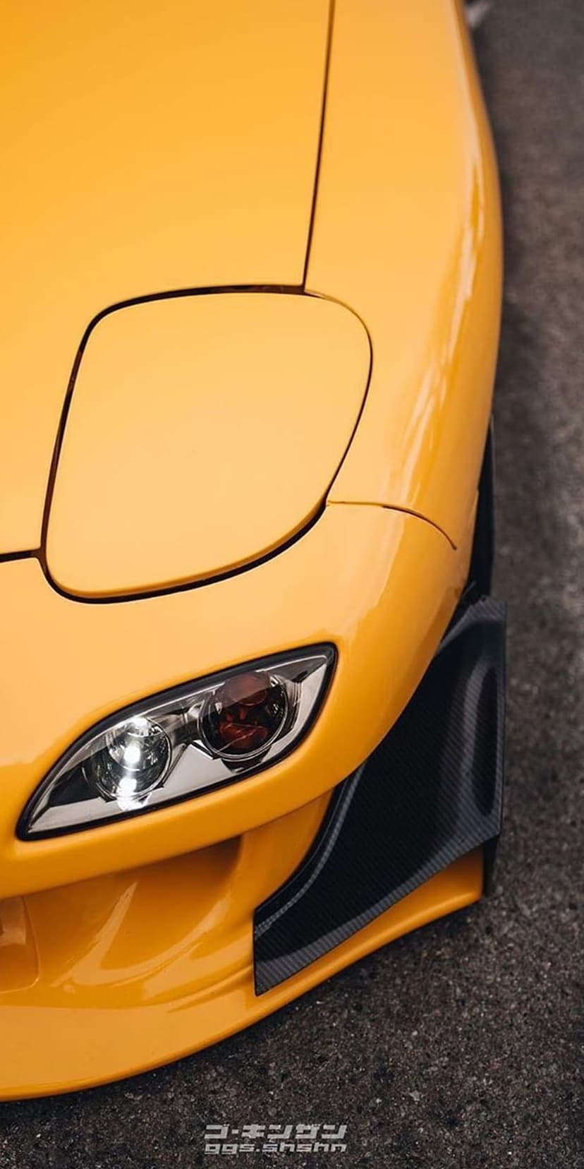 Yellow Mazda RX-7 FD headlight featuring dark carbon fiber splitters and textured front fender bodywork accents.