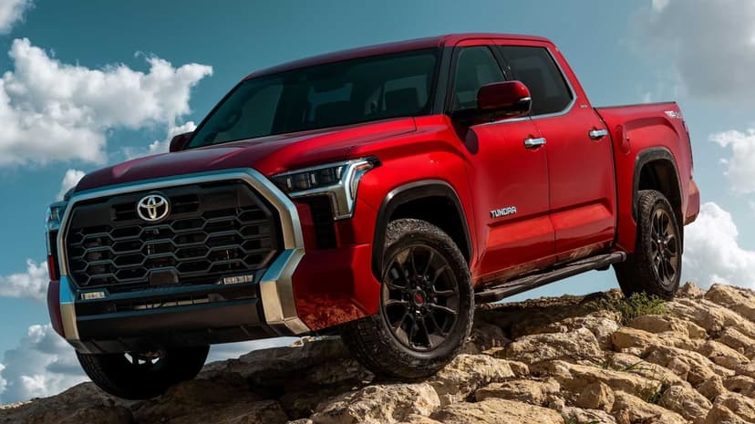 Red Toyota Tundra pickup truck perched on a rocky ridge against a bright blue sky filled with white clouds.