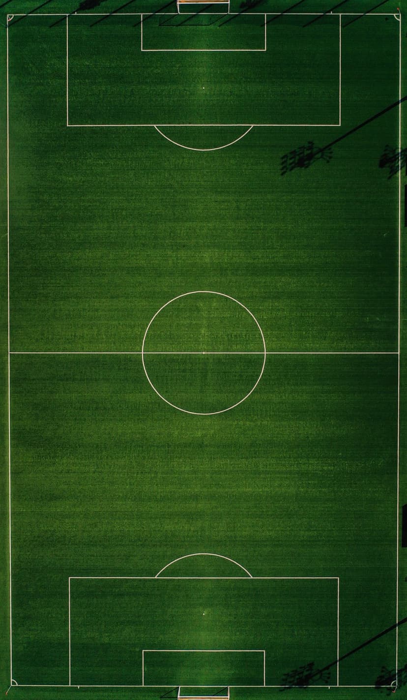Green soccer field from an aerial top-down view showing white boundary lines and long stadium light shadows.