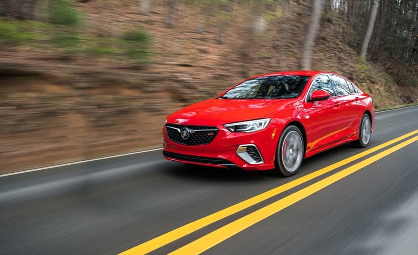 Red Buick Regal GS luxury sedan driving fast on a mountain road with motion blur and yellow lane markings.