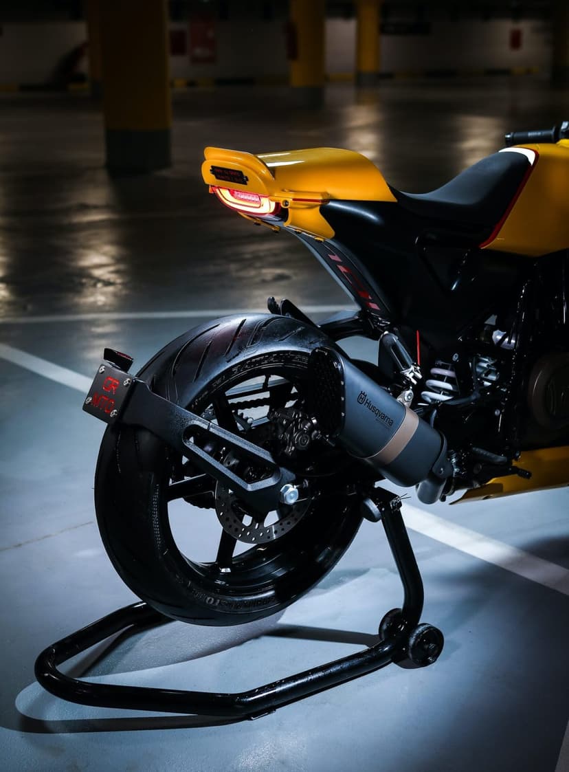 Rear view of a yellow Husqvarna motorcycle with a glowing tail light and matte exhaust in a dark garage setting.