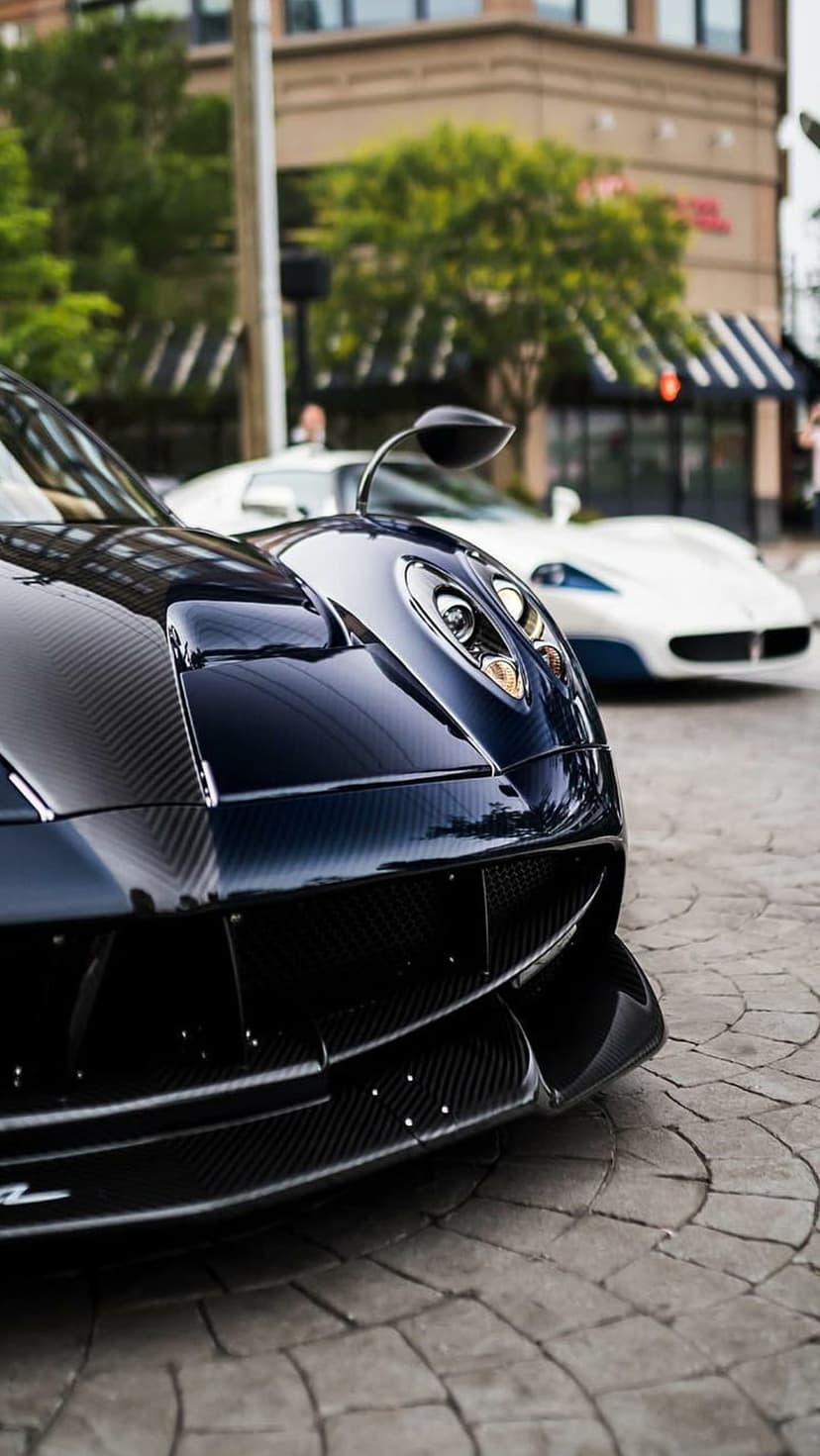 Pagani supercar front end with carbon fiber textures and distinctive headlights parked on a cobblestone street.