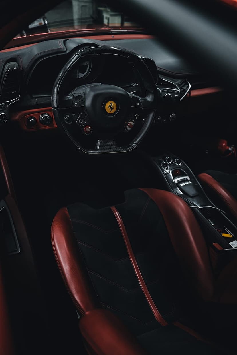 Red leather Ferrari seats and a steering wheel with the prancing horse logo inside a dark, luxurious cabin.