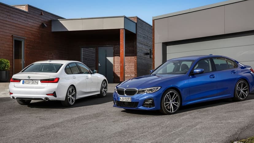 White and blue BMW 3 Series sedans parked in front of a modern wooden building under a clear blue sky.