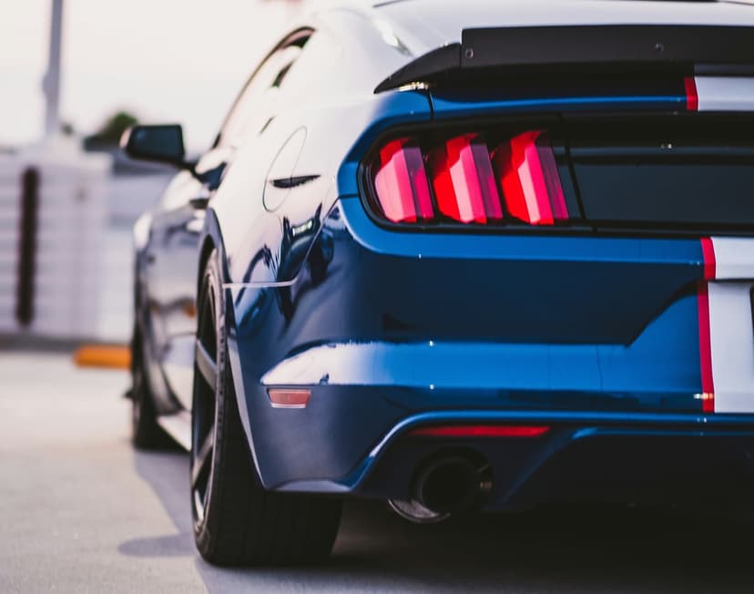 Blue Mustang rear with glowing triple LED tail lights, white racing stripes, and a sleek black spoiler wing.