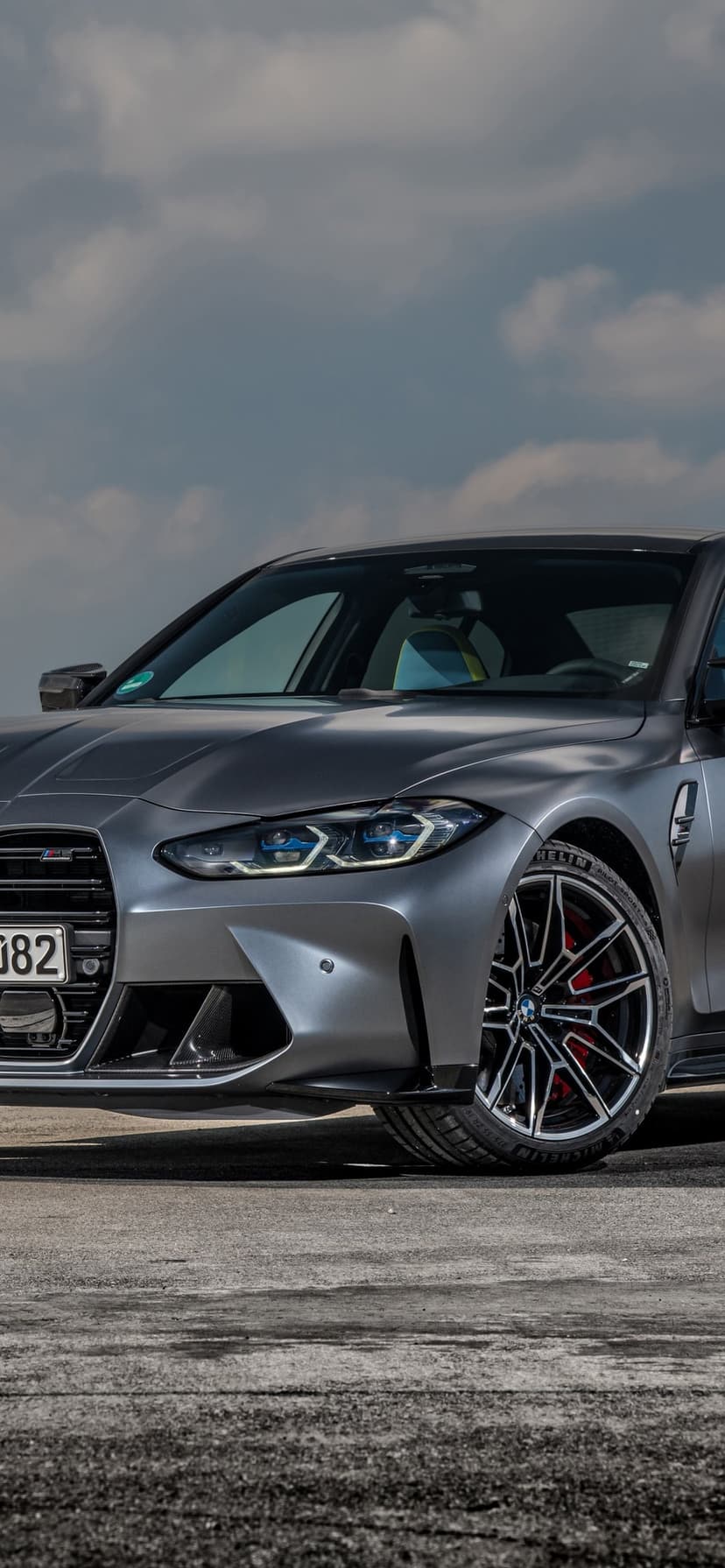 Front view of a matte grey BMW M3 with blue laser headlights, red brake calipers, and black alloy wheels.