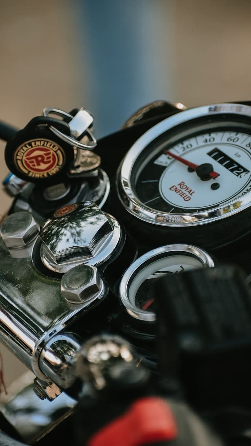 Royal Enfield chrome speedometer and branded ignition key positioned against a soft-focus motorcycle background.