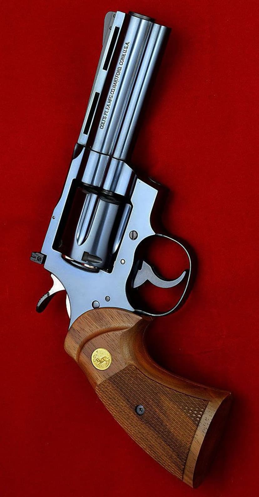 Colt Python .357 Magnum revolver with checkered walnut grips and gold inlay against a vibrant red background.