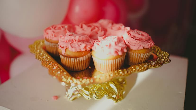 Pink frosted cupcakes with rose-swirled icing arranged on an ornate golden tray in a close-up vertical view.