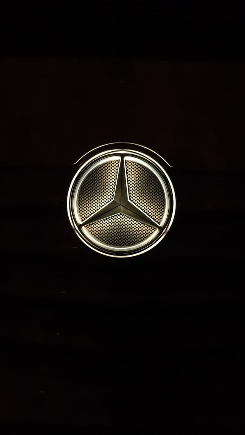 Mercedes-Benz three-pointed star logo glowing on a black textured grille with metallic silver highlights.