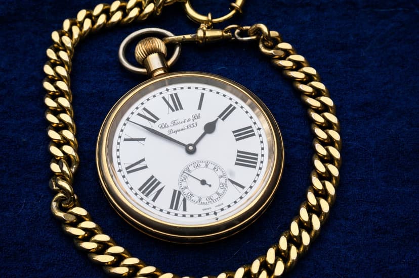 Gold pocket watch with Roman numerals and a thick ornate chain lies on a textured blue velvet background.