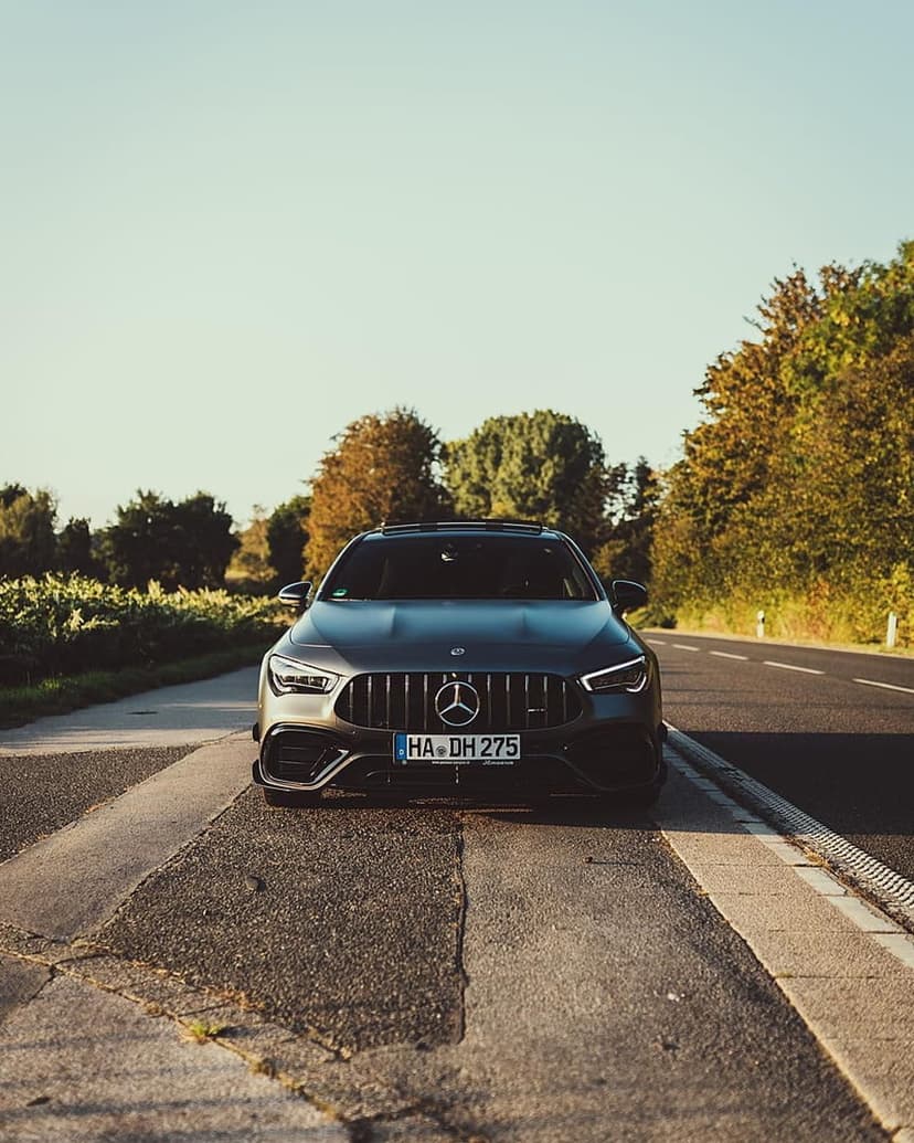 Mercedes CLA AMG luxury sedan parked on a sunlit roadside surrounded by vibrant green trees in the afternoon.