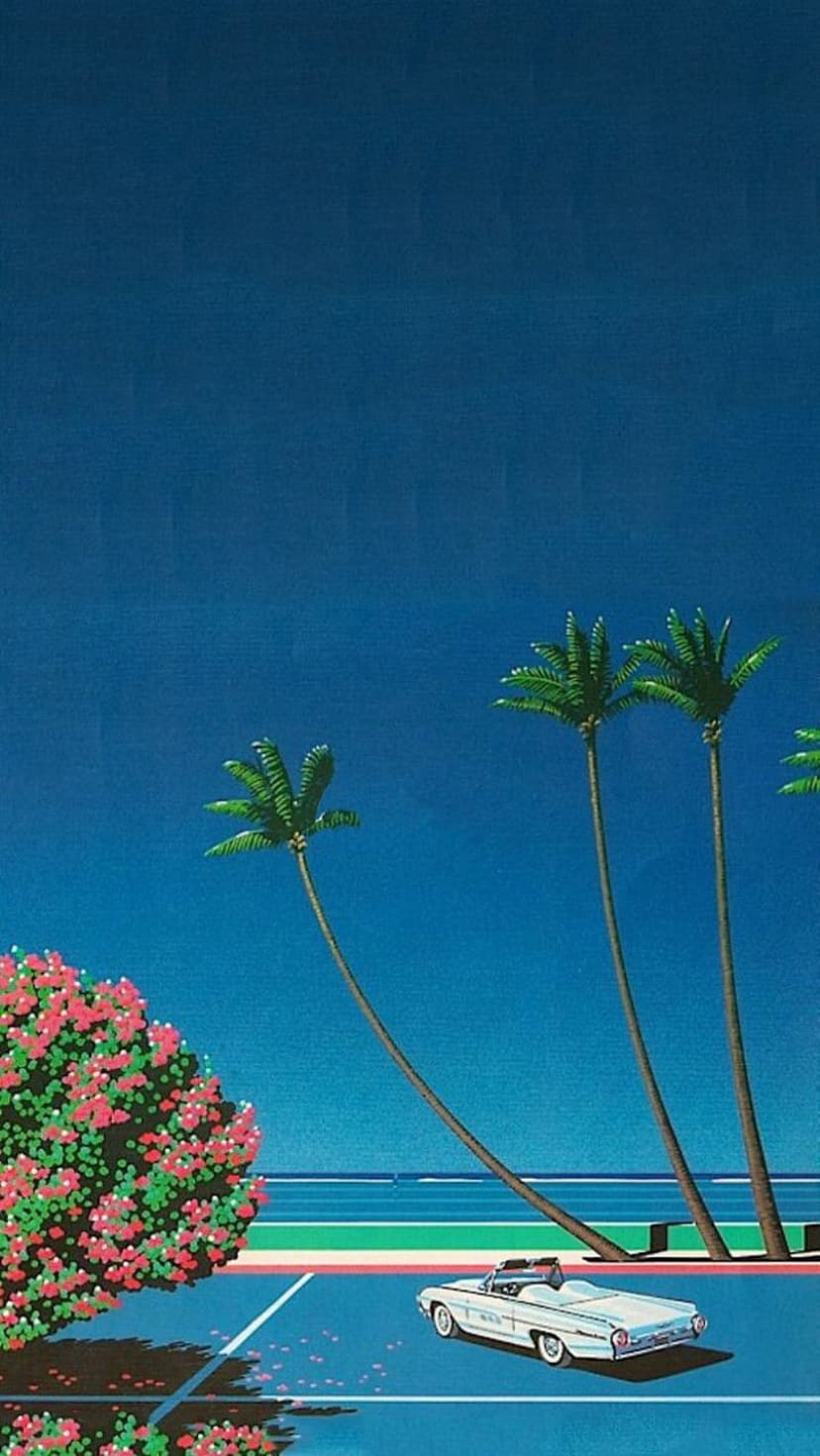 White convertible car parked next to pink flowering bushes and tall palm trees with a blue ocean background.