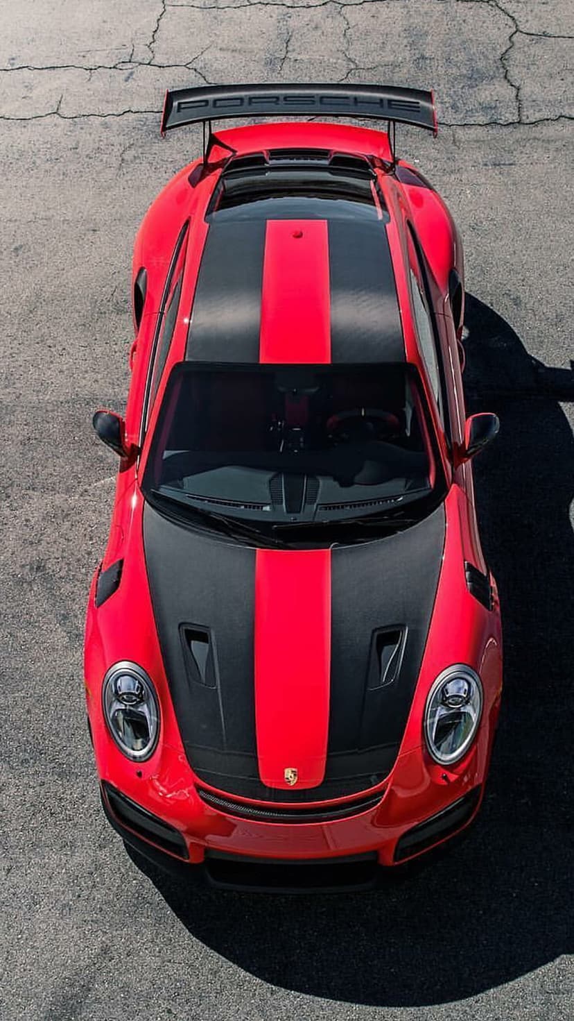 Red Porsche 911 GT3 RS seen from above showing black racing stripes and a carbon fiber wing on an asphalt track.