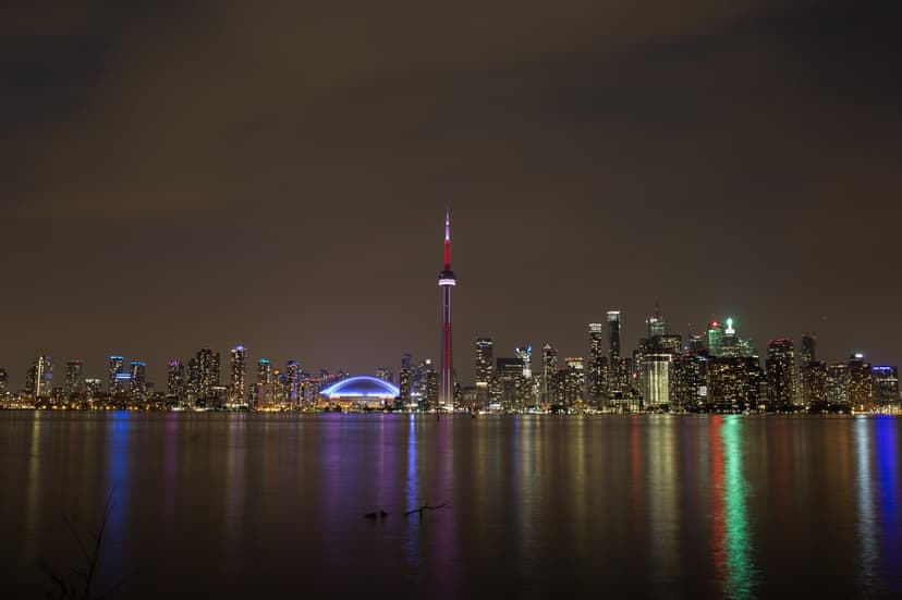 CN Tower and Toronto skyline reflected in dark lake water with glowing city lights under a clear night sky.