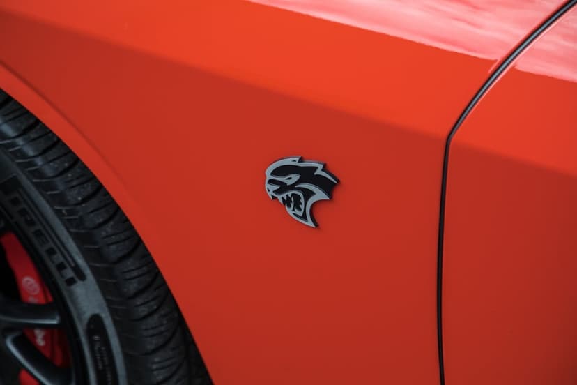 Hellcat emblem on a red Dodge Challenger fender beside a Pirelli tire and red brake caliper in sharp focus.