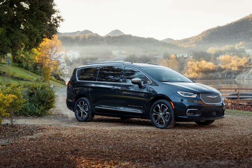 Dark blue Chrysler Pacifica Pinnacle on a gravel path by a misty lake with golden mountains in the background.