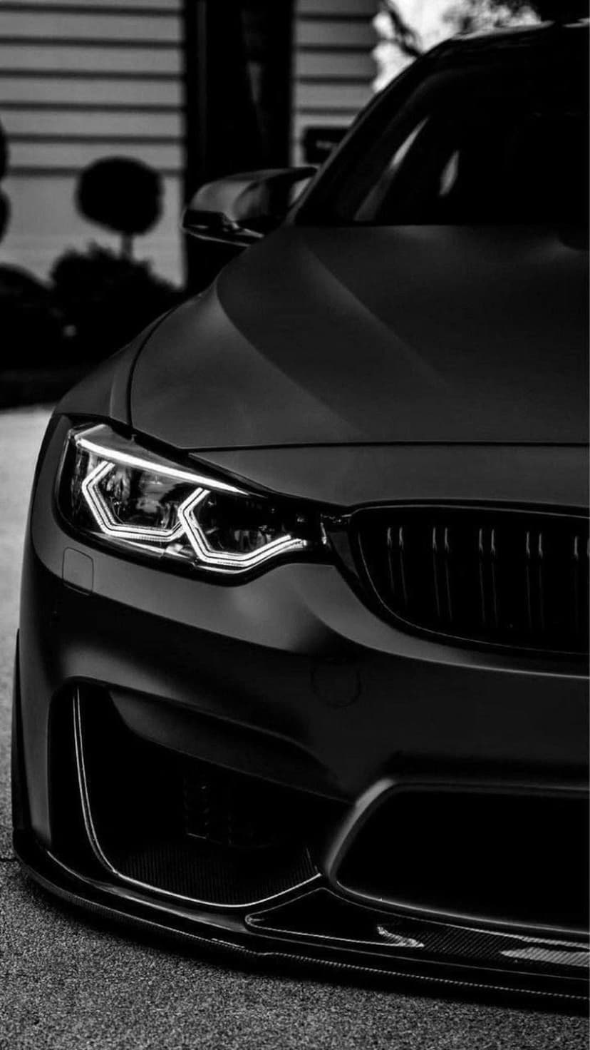 Matte black BMW headlight and kidney grille shown from a low angle with illuminated white LED lighting elements.