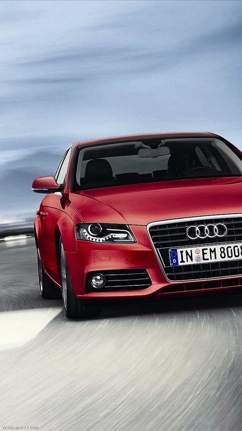 Red Audi A4 sedan driving fast on a wet road with glowing headlights under a dramatic sunset cloudscape.