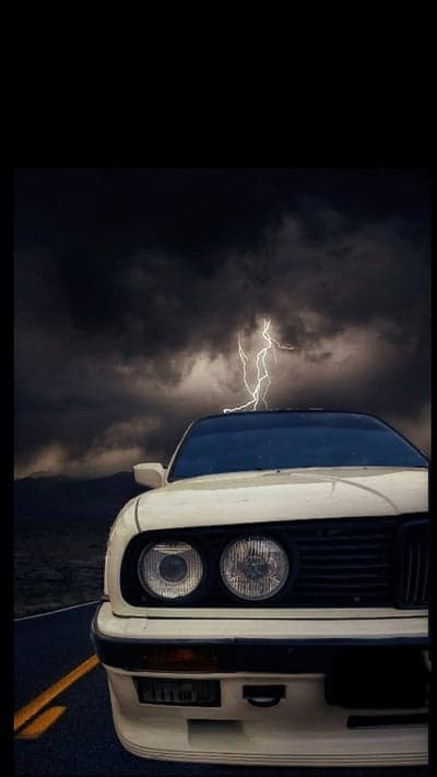White car under lightning storm on lonely road