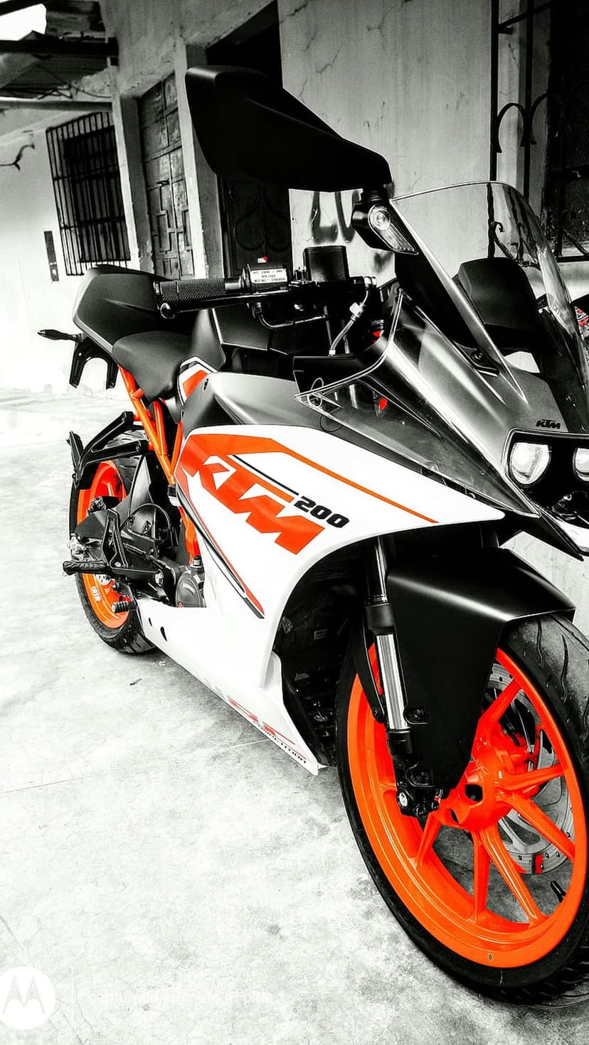 KTM RC 200 motorcycle with orange wheels parked against a textured wall and industrial metal floor grate.
