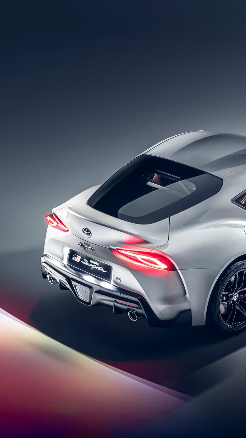 Rear view of a silver Toyota GR Supra with glowing red LED taillights in a dark minimalist studio setting.