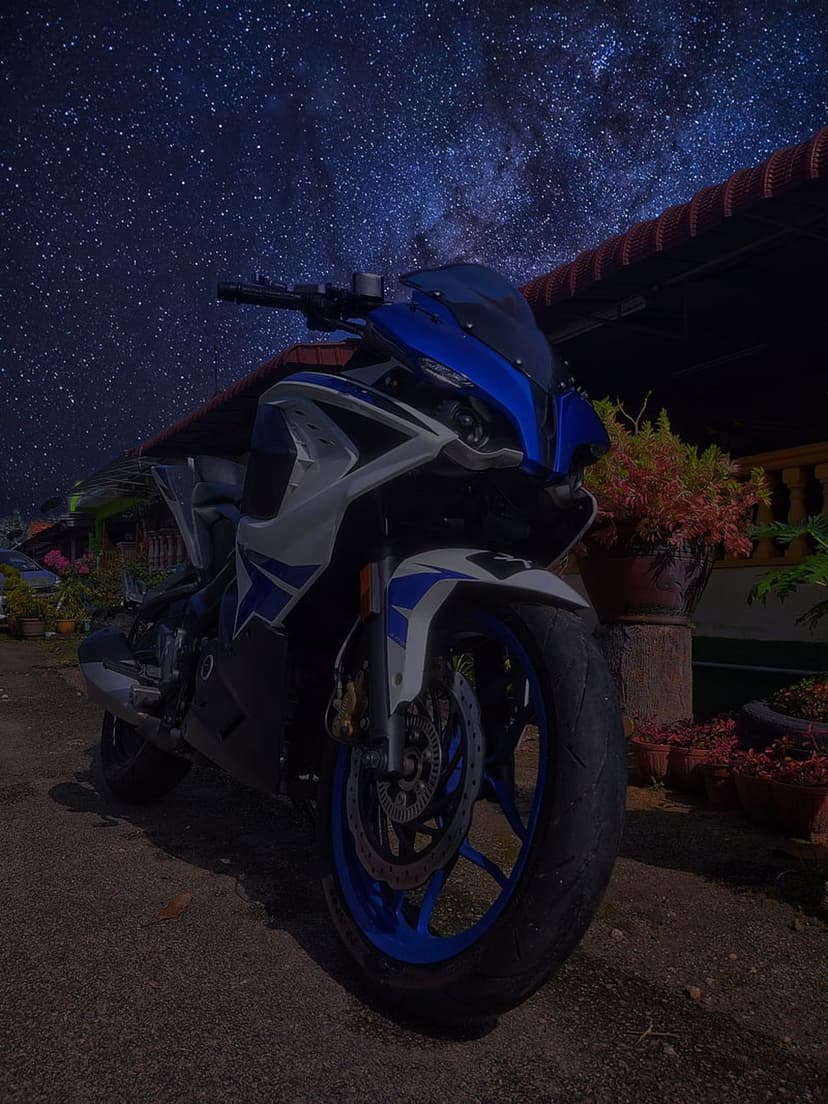 Blue and white sports motorcycle parked on dark ground under a brilliant Milky Way galaxy filled with bright stars.