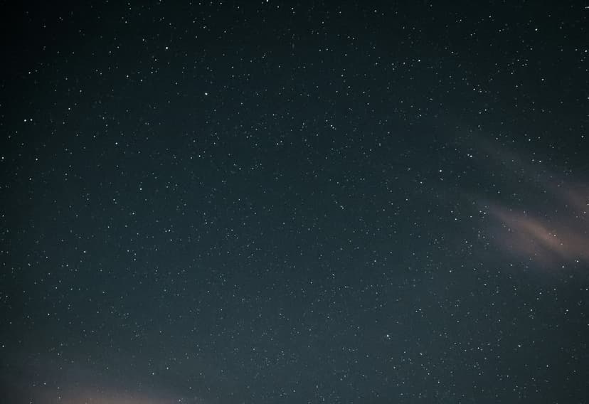 Starry night sky features shimmering constellations behind thin white clouds across a dark blue celestial backdrop.