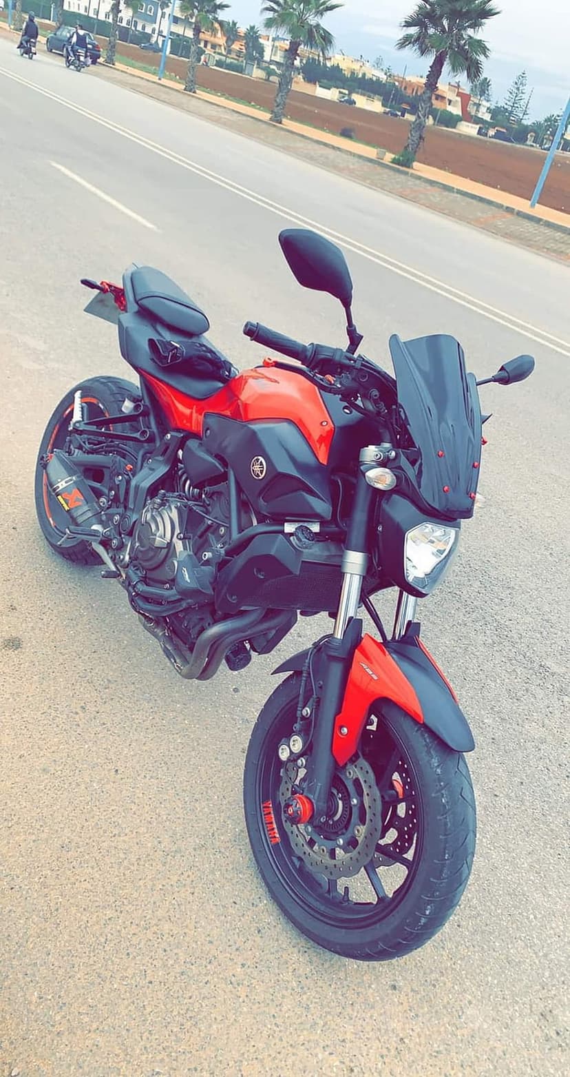Red Yamaha motorcycle parked on an asphalt street with green palm trees and city buildings in the background.